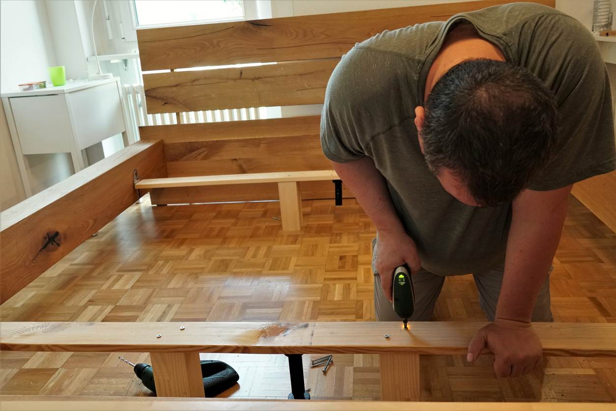 A man screwing screws in a wooden beams in assembling a new bed