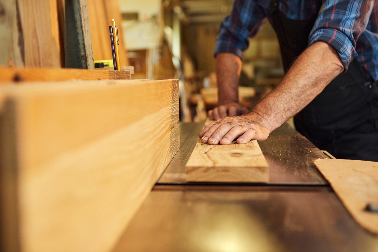 Senior carpenter in uniform works on a woodworking machine at the carpentry manufacturing